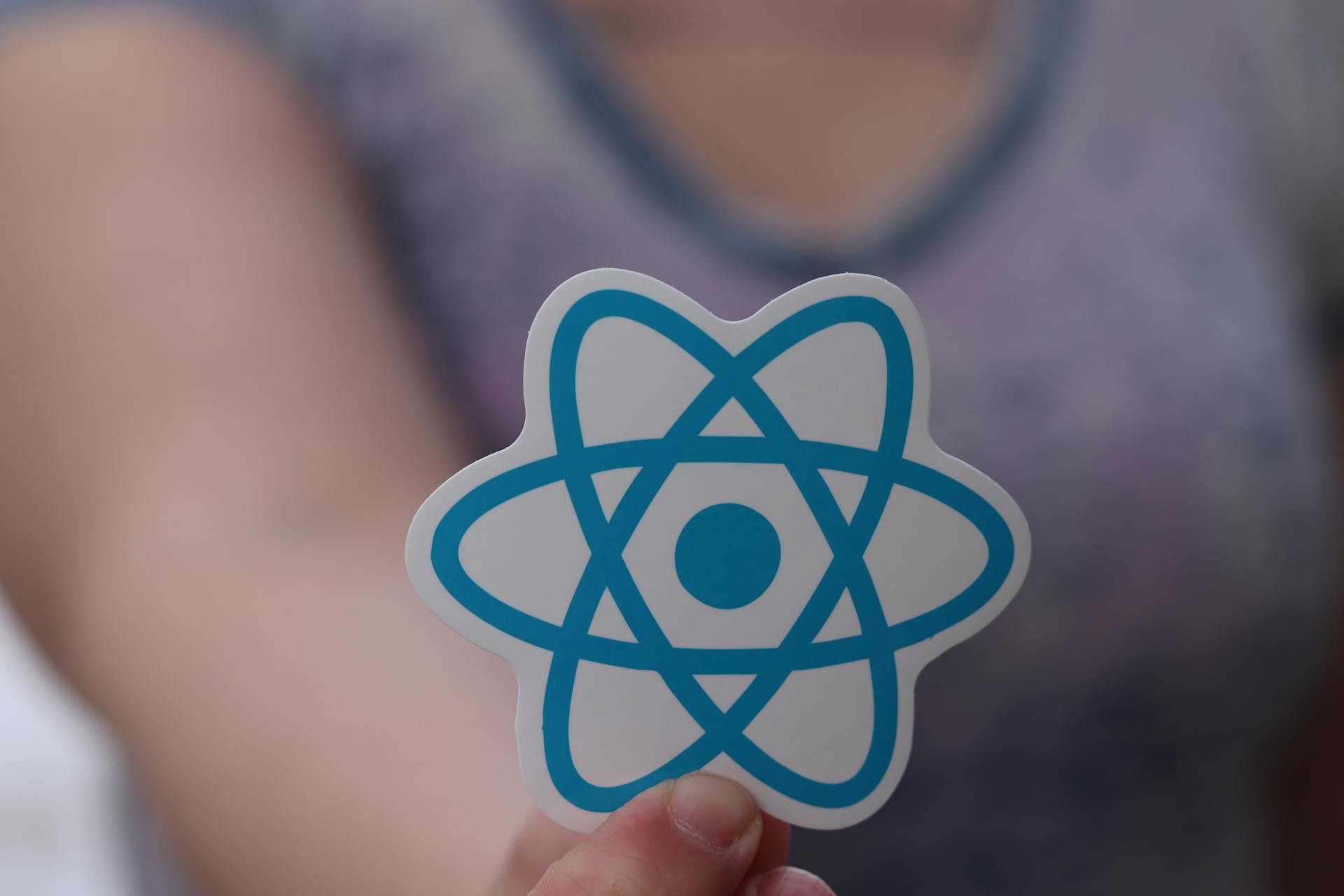 Person holding a sticker of React Native's logo close to the camera.