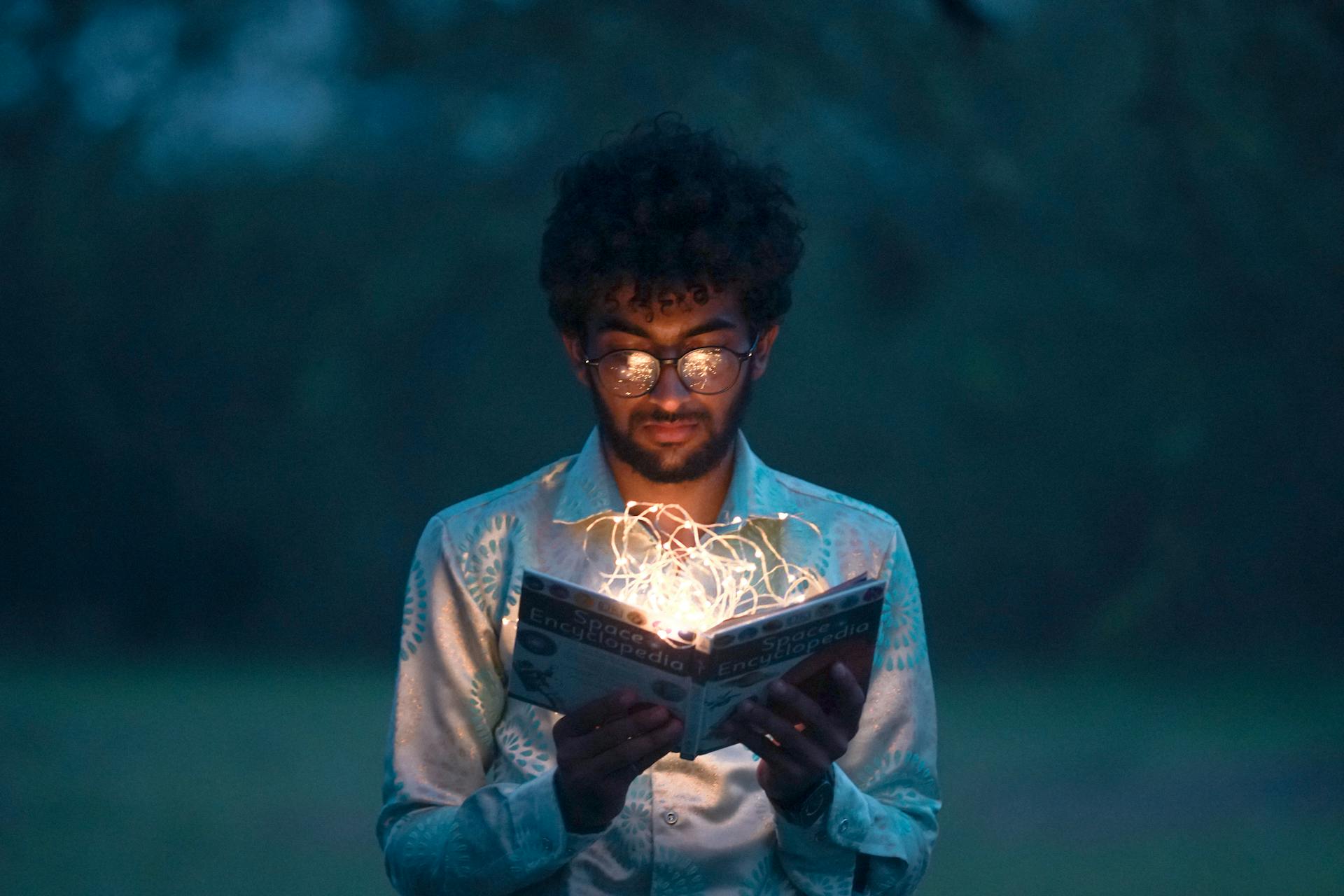 Man holding book that is glowing with fairy lights.